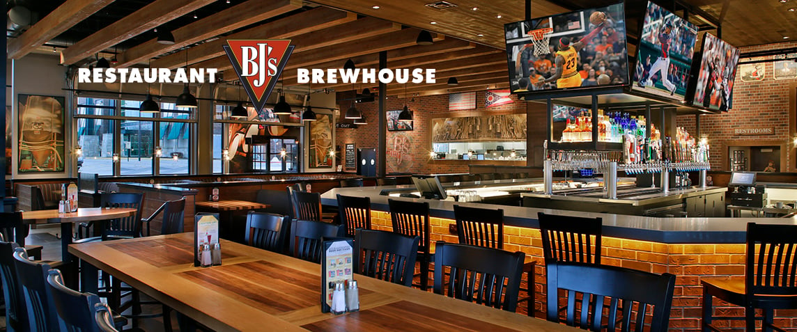 Inside of a BJs brewhouse and restaurant, with a large bar and sports displayed on the tv screens