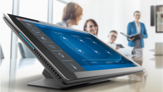 Q-SYS TCS Series touch pane on a conference table with employees conducting a conference call in the background